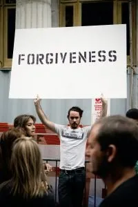 A man holding up a sign that says forgiveness in a crowd of people