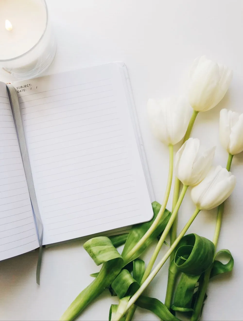 A blank journal on a desk with white tulips beside it