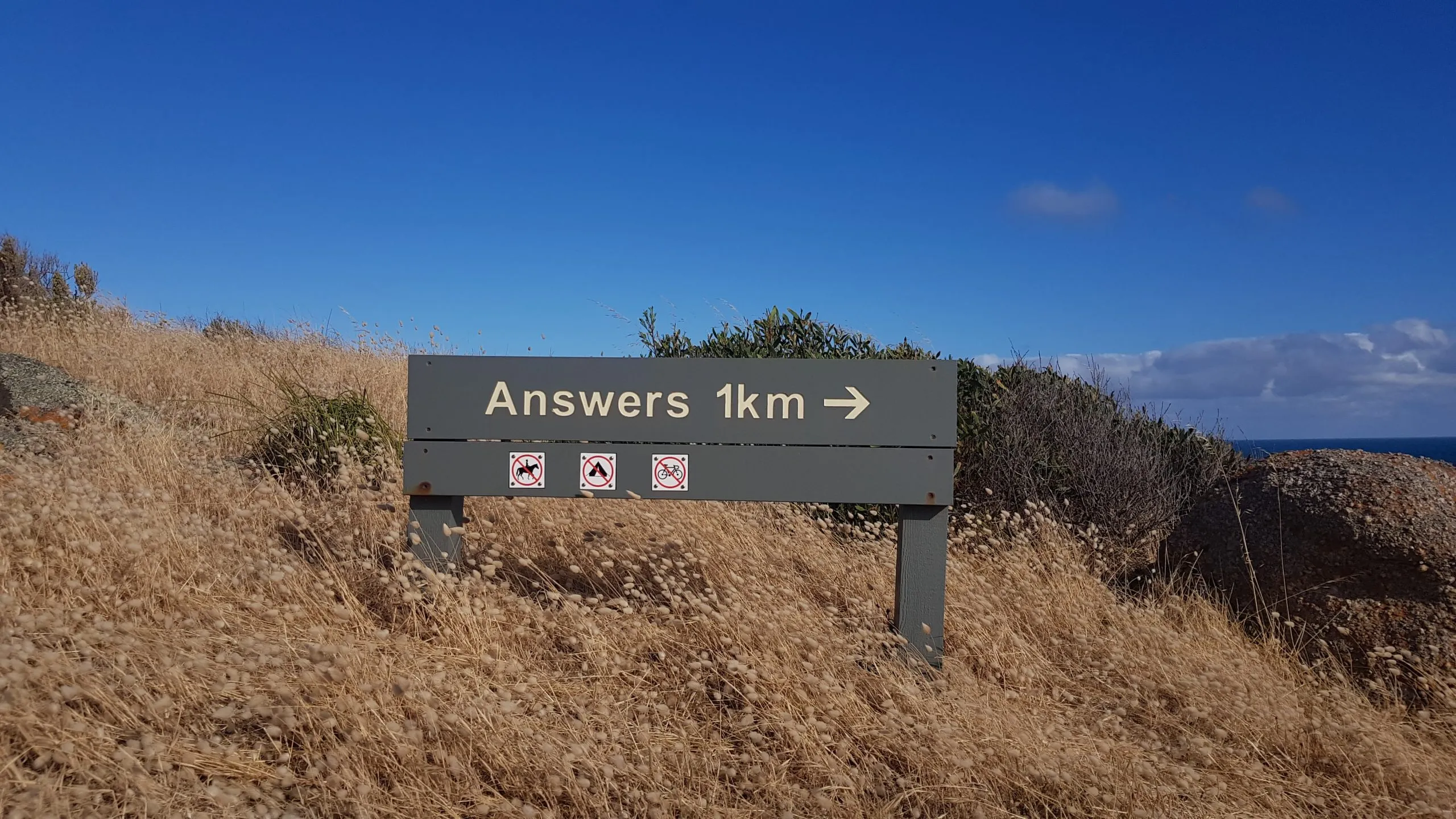 A wooden road sign that direct you to Answers 1 km that way