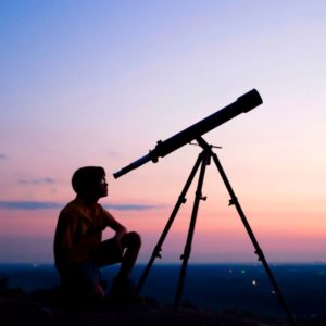 Boy looking through a telescope at dusk
